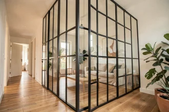 Verrière intérieure en acier noir avec panneaux de verre séparant un salon et un couloir dans un appartement moderne