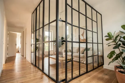 Verrière intérieure en acier noir avec panneaux de verre séparant un salon et un couloir dans un appartement moderne